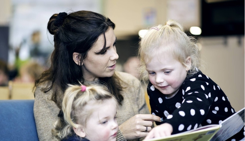 Vrouw laat aan twee kinderen een boek zien.