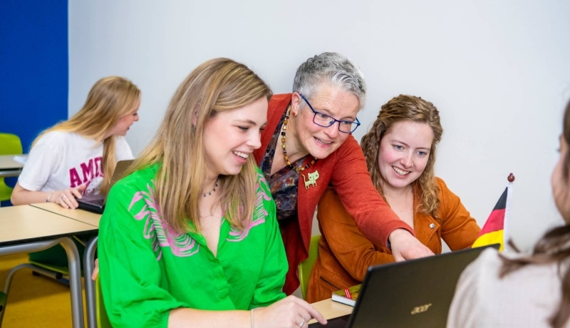 Lerarenopleider helpt twee studenten door iets aan te wijzen op de laptop die voor hun staat.
