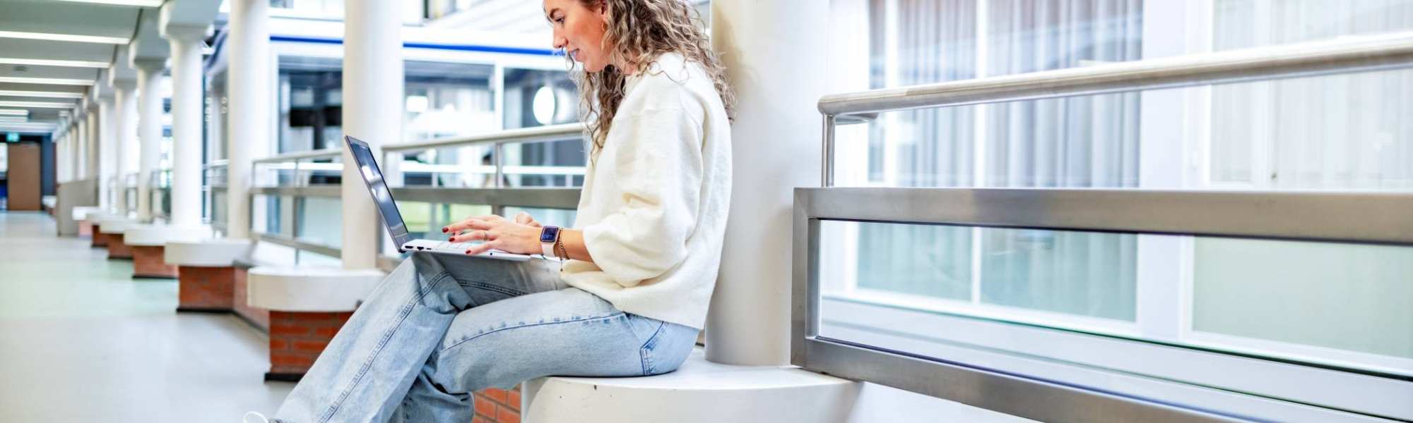 Student van de bachelor Commerciële Economie deeltijd, duaal in gang met laptop.