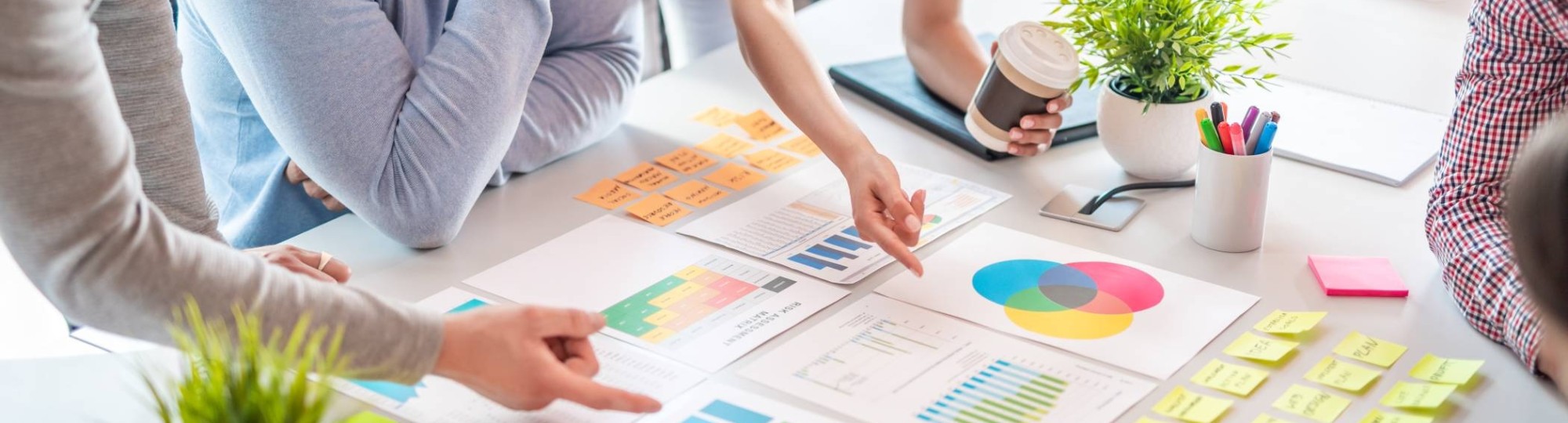 Sfeerbeeld van collega's die samenwerken aan een tafel met post-its, schema's en tabellen 