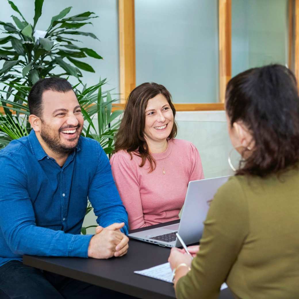 Drie master studentes zitten lachend aan tafel.