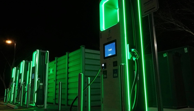 Foto met daarop groen verlicht elektrisch laadstation. Op een van de units staat electrify america