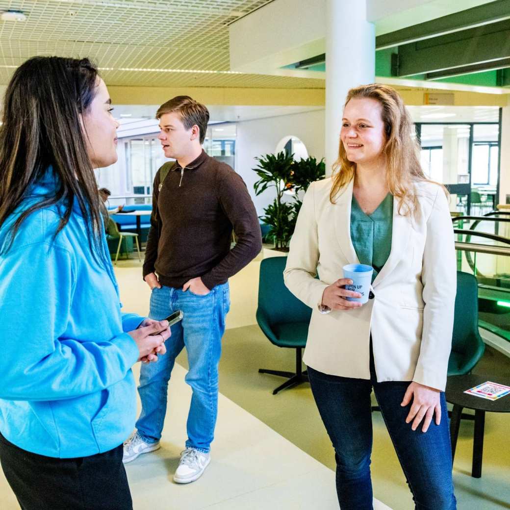 Studenten en docent Bedrijfskunde voltijd samen in gesprek in de gang van het gebouw