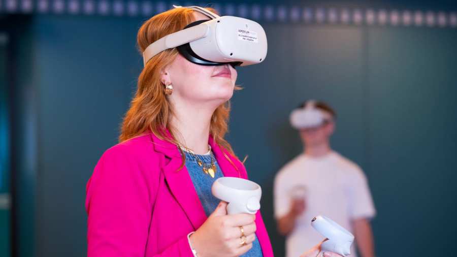 Studente oefent met VR bril, jongen wacht op de achtergrond
