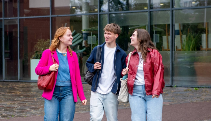 2 meiden en een jongen kijken elkaar aan en lopen bij de hoofdingang van de HAN campus naar buiten