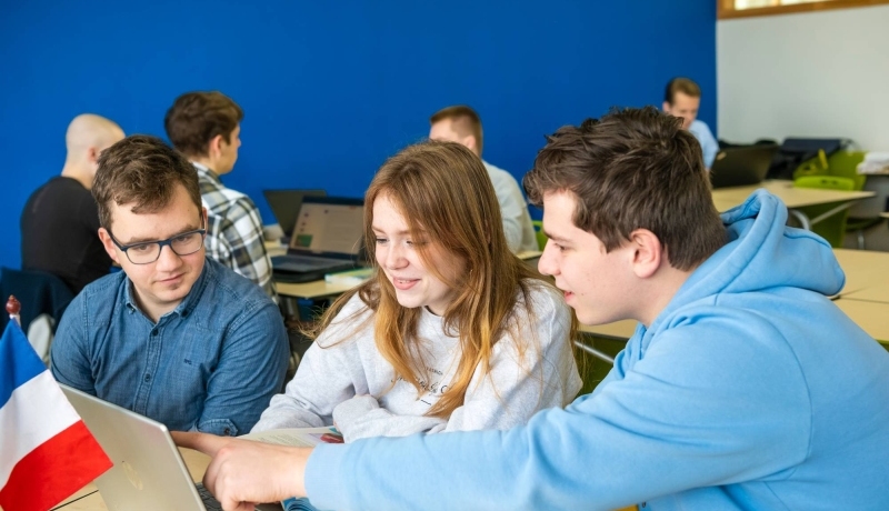 Drie studenten Leraar Frans krijgen uitleg van hun docent die tussen hen in staat.