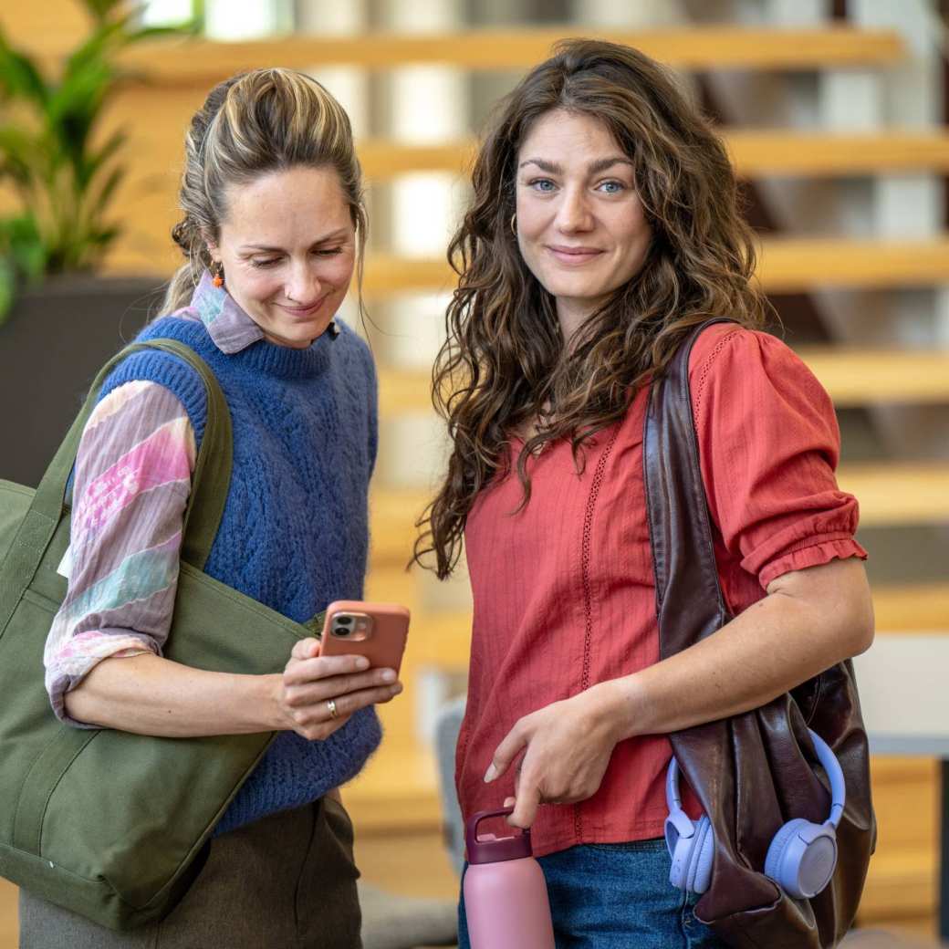 Twee studenten op de campus en 1 student kijkt op telefoon
