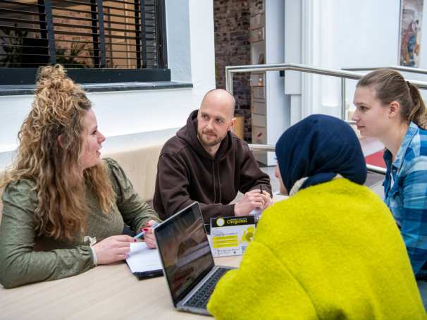 Een groep van 4 studenten overleggen aan zittend een tafel.
