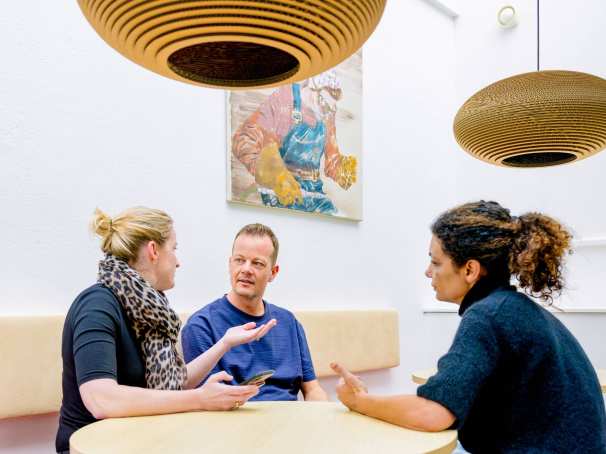 Vrouw legt iets uit aan man en vrouw tijdens de cursus acute pijn service. Dit doet ze in de kantine.