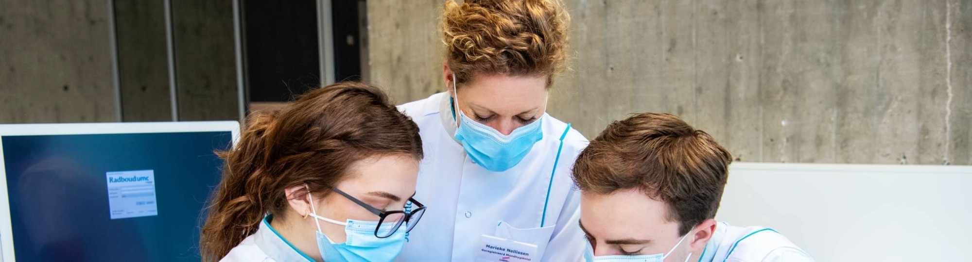 2 studenten en een docent kijken in de mond van een patient op een behandelstoel.
