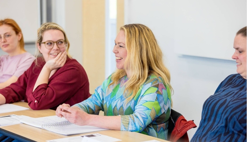 Vrouw is in gesprek en aan het lachen tijdens de cursus acute pijn service. Andere vrouw kijkt haar aan op de achtergrond.