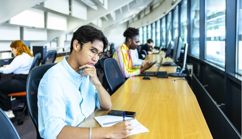 Studenten aan het werk op telefoon of laptop in de bibliotheek.