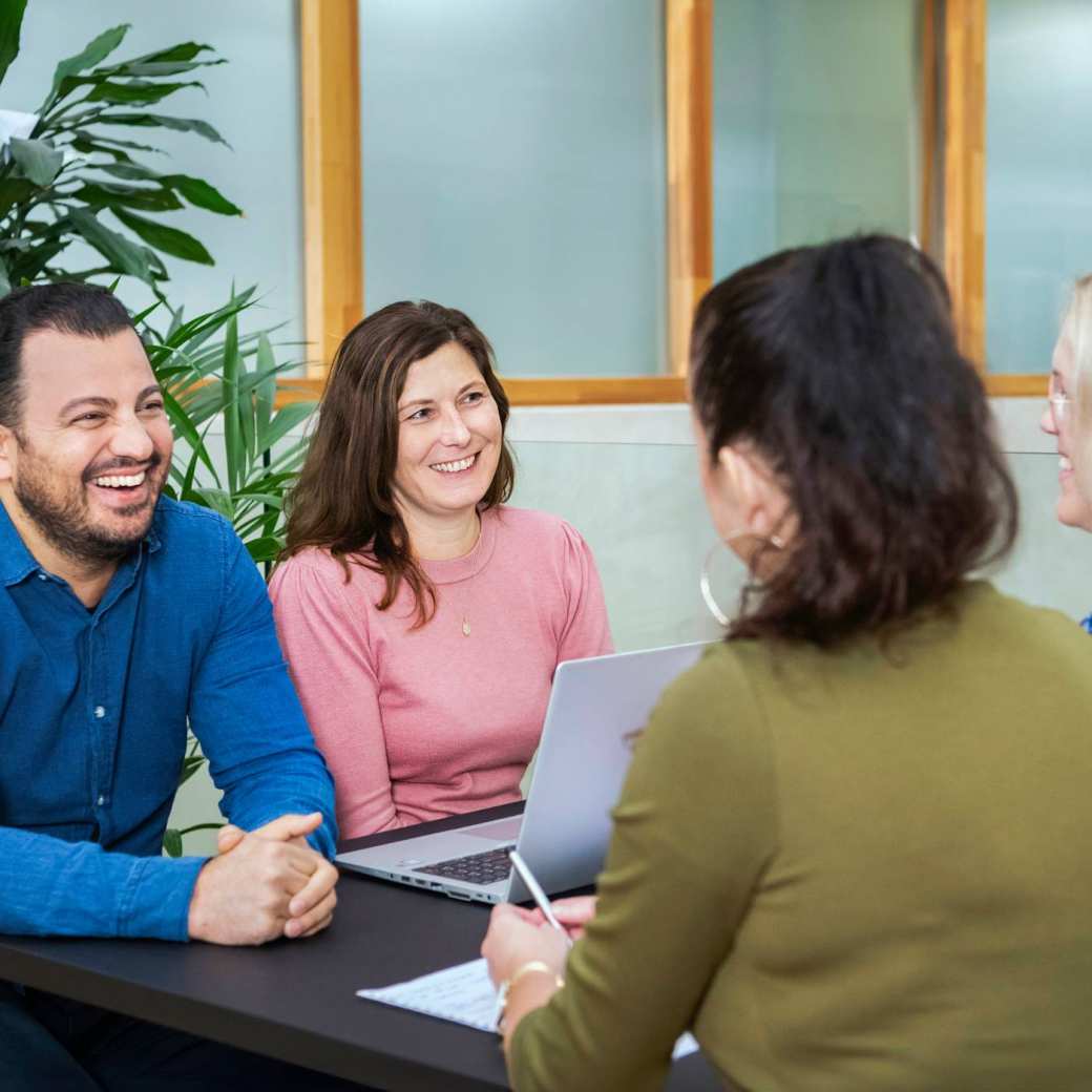 Drie master studentes zitten lachend aan tafel.