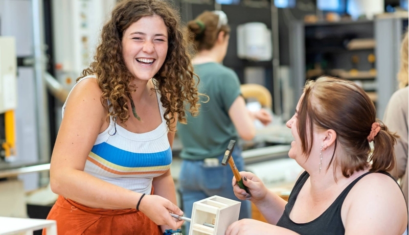 Twee beeldende therapie studenten werken samen aan een project in houtlokaal tijdens een praktijkles