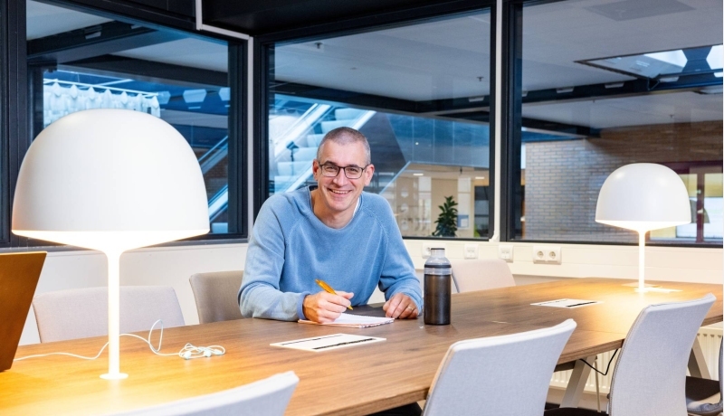 Guus Witjes zit aan een tafel en schrijft