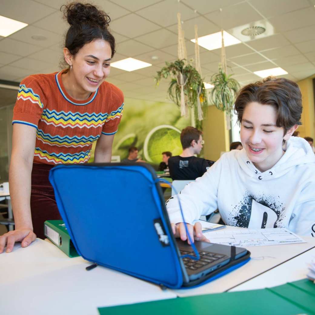 jongen werkt op laptop terwijl zijn docent helpt
