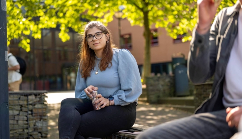 Portretfoto van studente buiten zittend op een bankje bij K33, in de pauze. 