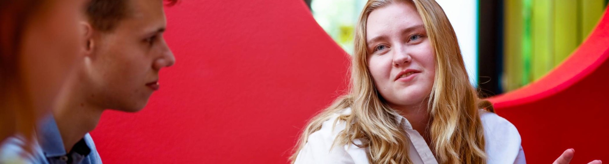 Jonge vrouw met blond haar en witte blouse heeft een marker in haar hand en praat met 2 jongens