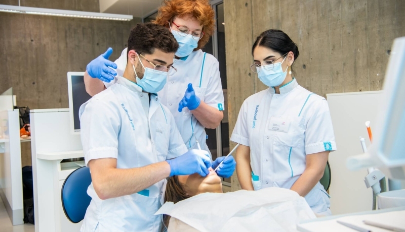 Docent helpt een student tijdens een behandeling, een andere student kijkt toe.