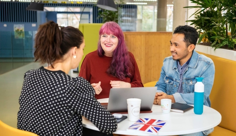 Drie studenten Leraar Engels zitten aan een ronde tafel te overleggen met elkaar.
