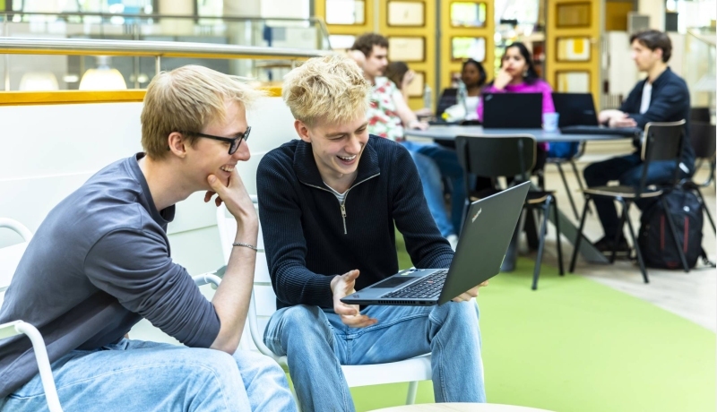 Twee hbo-ict studenten kijken samen lachend naar hun laptop