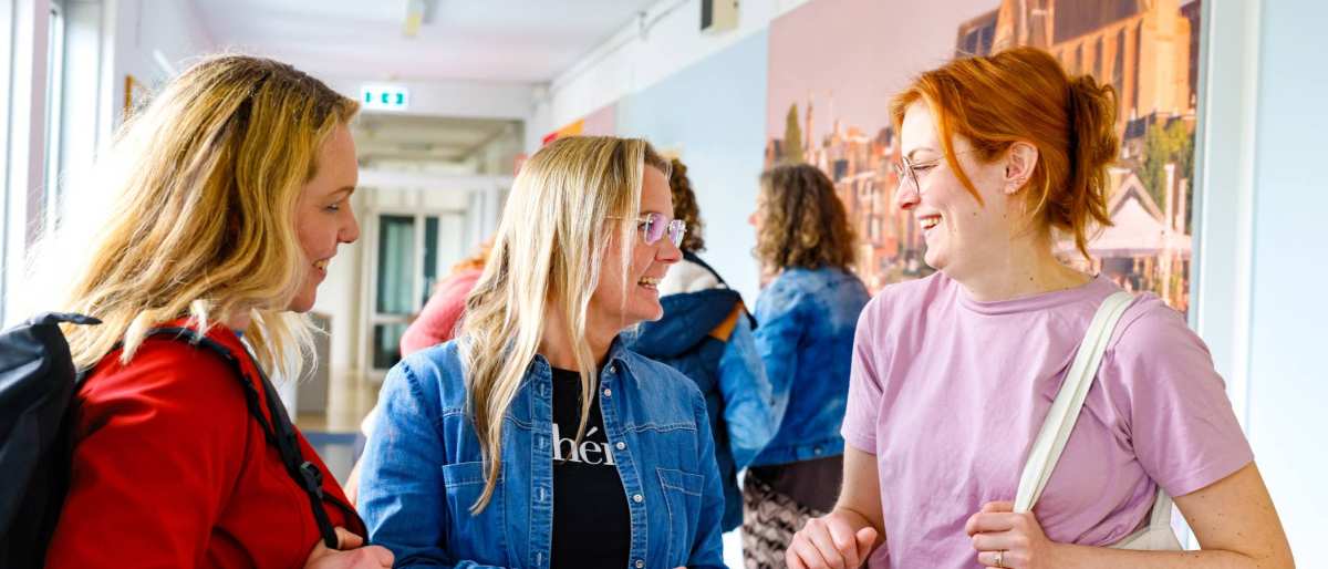 Vrouw laat iets zien op haar mobiel tijdens de cursus acute pijn service. Andere studenten moeten lachen.