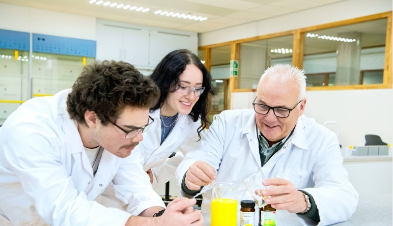Twee studenten in een labjas kijken aandachtig naar een reageerbuisje.