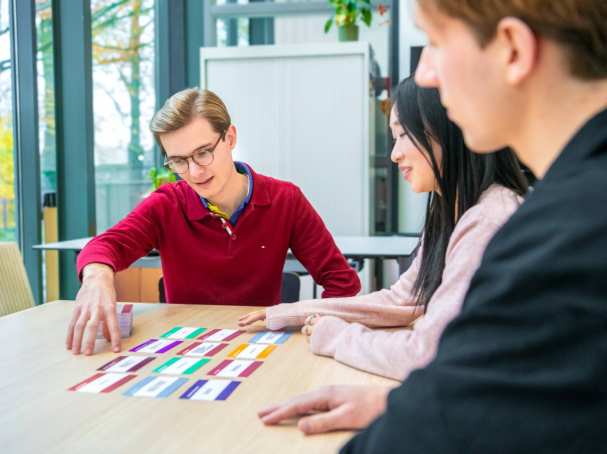 Drie mensen zitten aan tafel en kijken naar gekleurde kaartjes die gesorteerd op tafel liggen