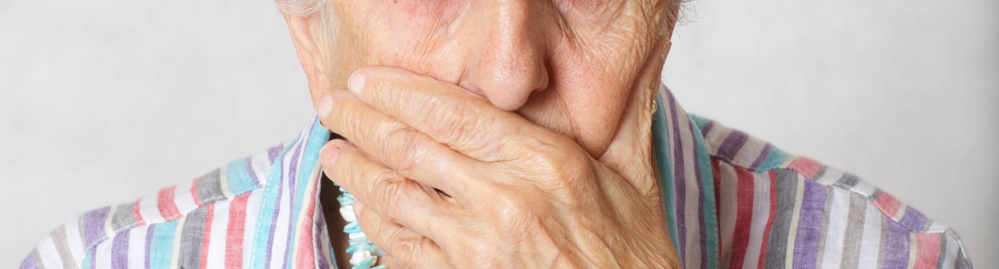 Oude dame met haar hand voor haar mond.