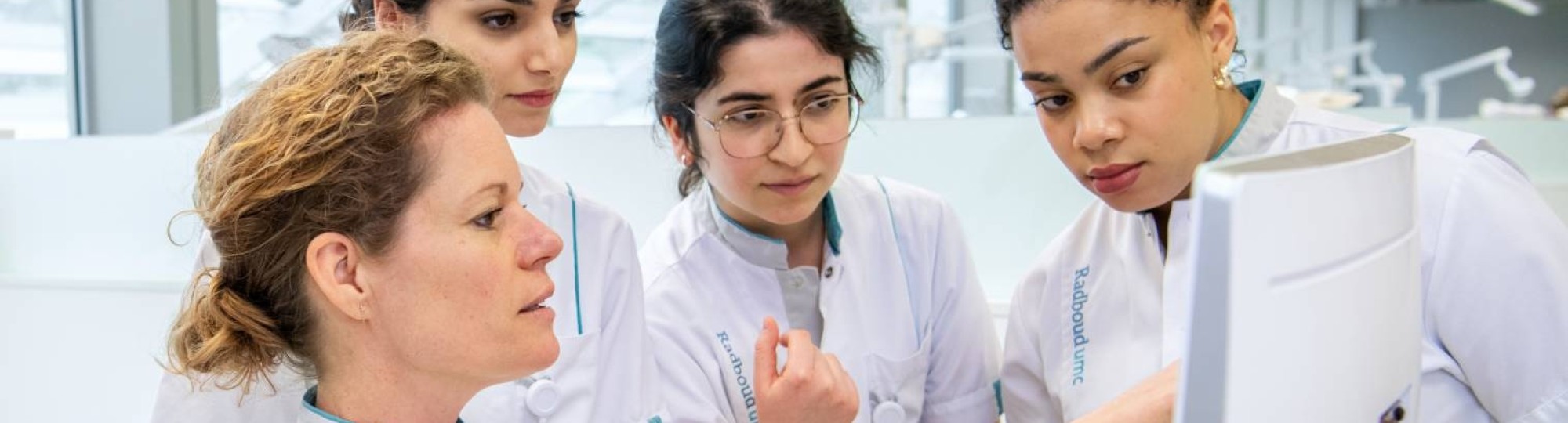 Docent laat wat zien op de computer, de studenten kijken allen toe.