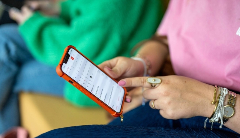 Student houdt haar telefoon vast en wijst er met haar vinger iets op aan. 