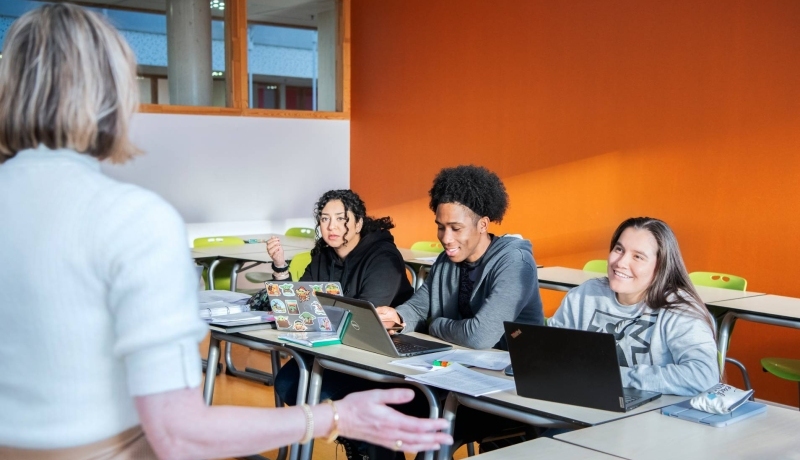 vier masterstudenten aan tafel moeten lachen en kijken elkaar aan.