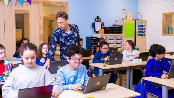 Groep 5,6,7 op de school Da Vince. De leerlingen zitten in de klas achter de laptop terwijl de leraar rond loopt. 
