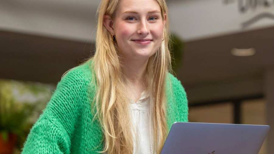Studente lacht in de camera, heeft laptop op schoot en is aan het werk bij The Brew.