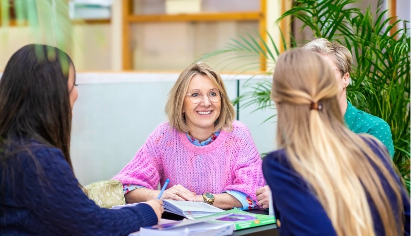 Een man en een vrouw kijkend naar een schrift op tafel in een klaslokaal