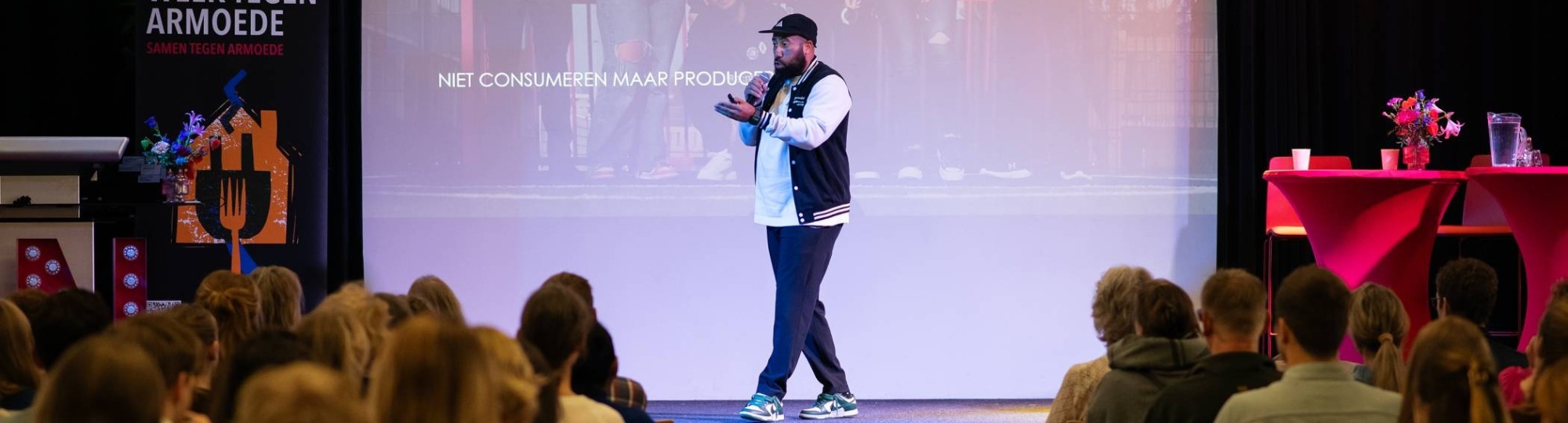 Volle zaal in Nijmegen met mensen in stoelen met voorraan een podium waarop Melvin Kolf, een jongen met een petje en baseball pet, zijn verhaal doet over Presikhaaf University