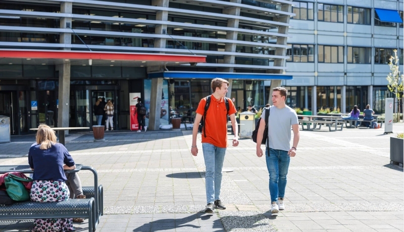Twee studenten lopen lachend buiten op het plein voor de campus in Arnhem