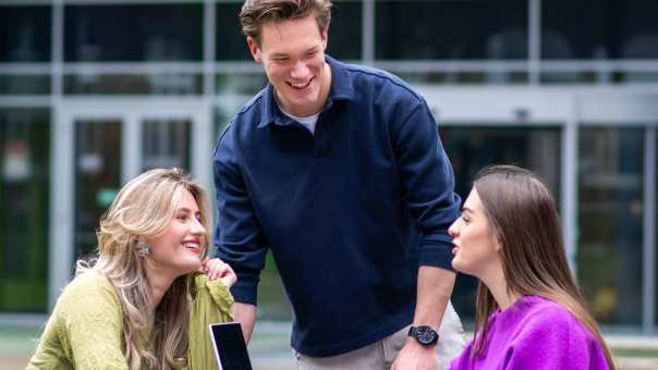 Drie studenten van Learning and Development in Organisations voltijd in gesprek buiten op een bankje voor Laan van Scheut 10 in Nijmegen.