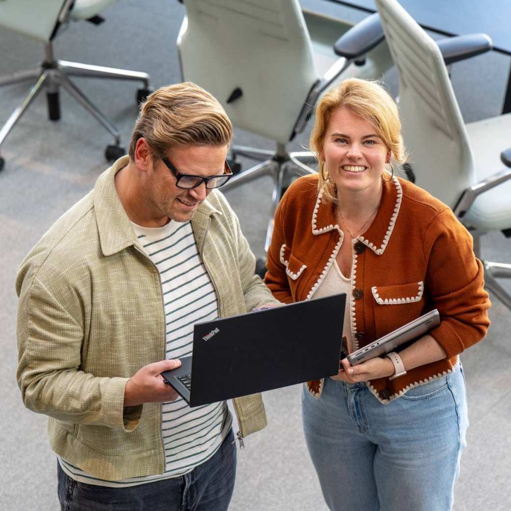 Man en vrouw staan met laptop in de hand en kijken lachend naar camera