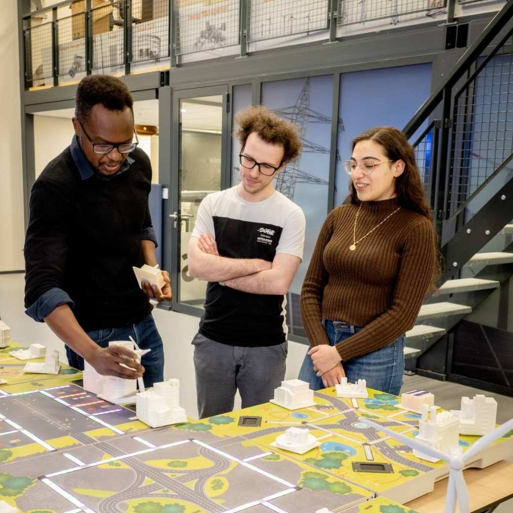 Twee studenten van de Master Engineering Systems Sustainable Energy en een docent bij de Smart Grid-demotafel.