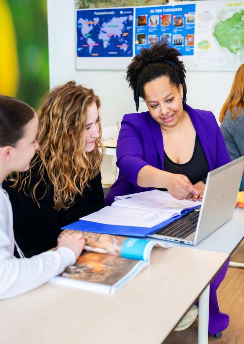 Docente Angel Olatunji geeft uitleg aan 2 middelbare scholieren die aandachtig kijken terwijl zij op het laptopscherm wijst, op het Citadel College. 