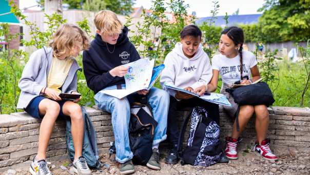 Vier leerlingen lezen buiten op een bankje. Foto van de opleiding leraar basisonderwijs