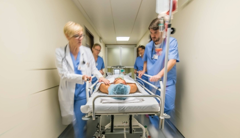 Medewerkers van de spoedeisende zorg lopen met spoed met een patiënt in bed door de gang van een ziekenhuis.