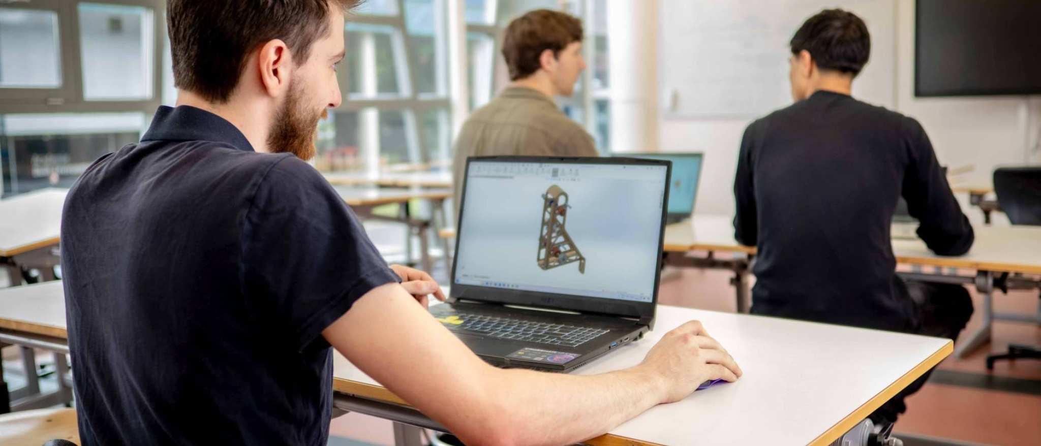 Een student werktuigbouwkunde 3D-tekent op zijn laptop in het klaslokaal.