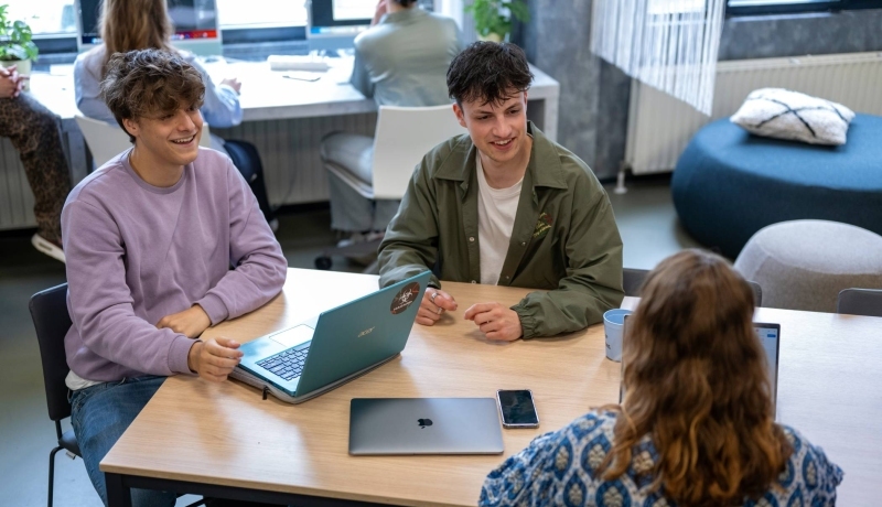 Studenten zitten in een klas en werken samen aan tafel, ze hebben plezier.