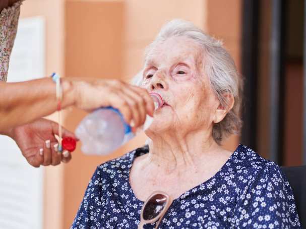 Een oude vrouw drinkt uit een flesje.