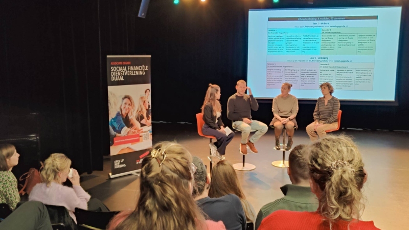 sfeerbeeld van dialoogsessie werkveldpartners sociaal financiële dienstverlening met op het podium docenten en student Daan