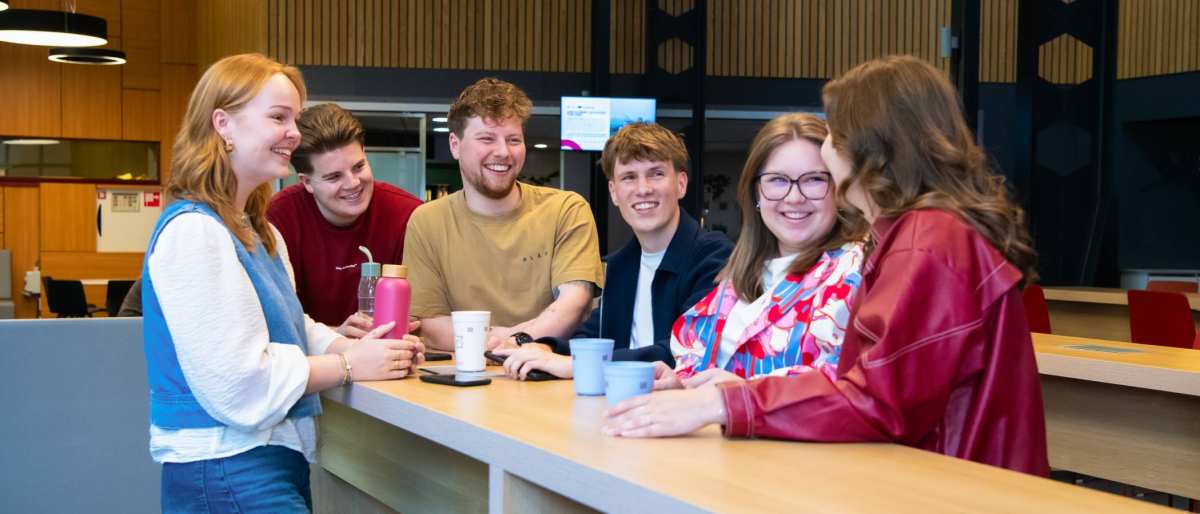Studenten praten met elkaar aan de uitleenbalie van Ergotherapie met koffie en thee.