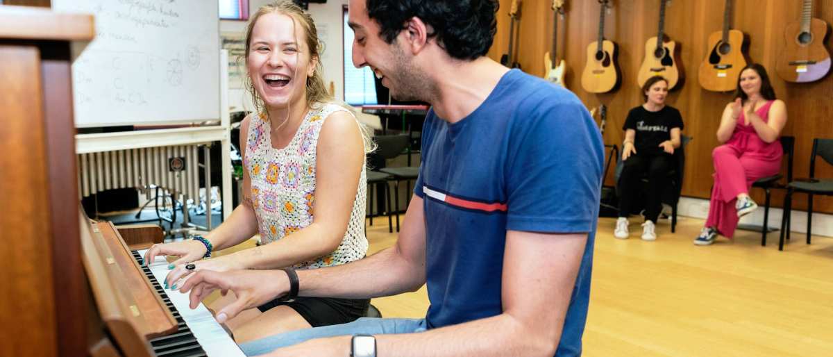 Twee studenten spelen op piano in muzieklokaal