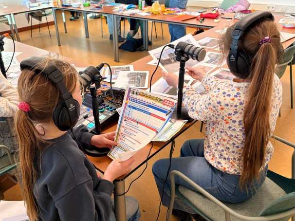 Foto van twee meisjes (met koptelefoons en foto's uit hun buurt) in gesprek met professionals over hun leefomgeving